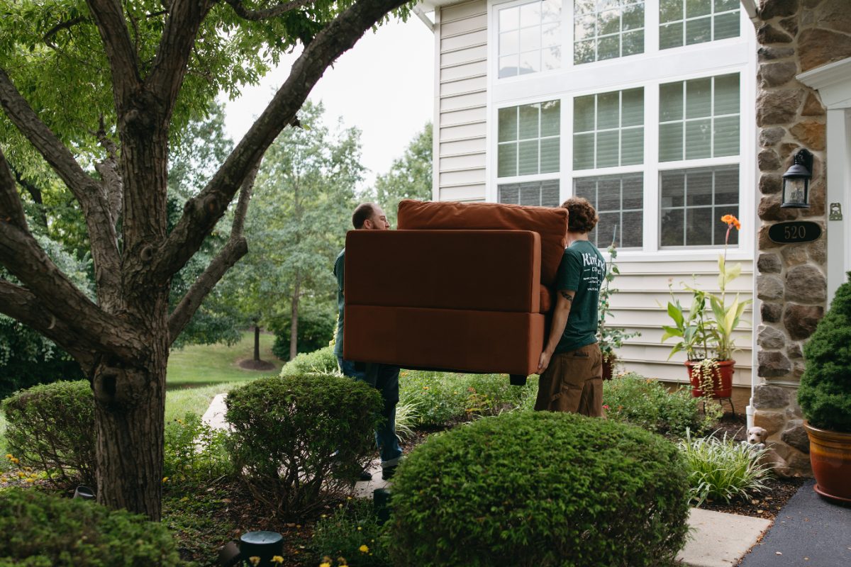 Two Kindred team members carrying a sofa up a customer's front walk